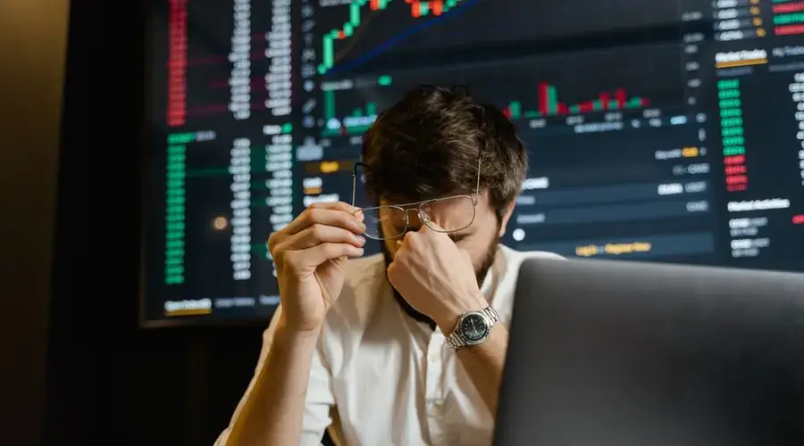 A stressed man looks at stock market data on his computer screen in an office setting.