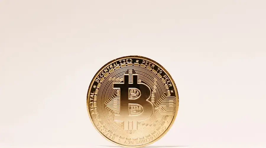A golden Bitcoin coin standing upright against a minimalist light background.
