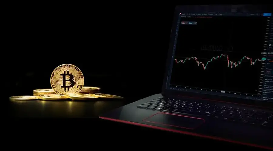 Golden bitcoin coins next to a laptop displaying a trading graph, symbolizing digital currency investment.