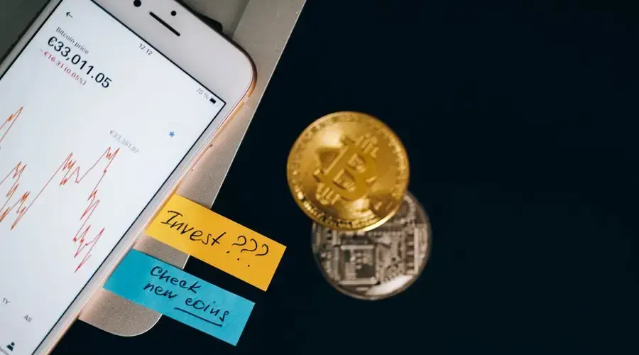 Bitcoin coins and smartphone displaying price chart with investment notes.
