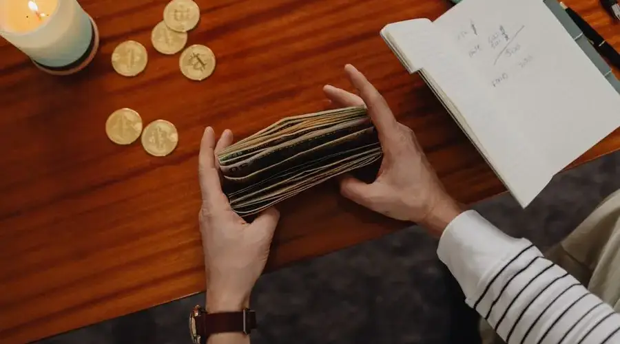 Close-up of a person organizing money with cryptocurrency coins on a wooden table, symbolizing modern finance.