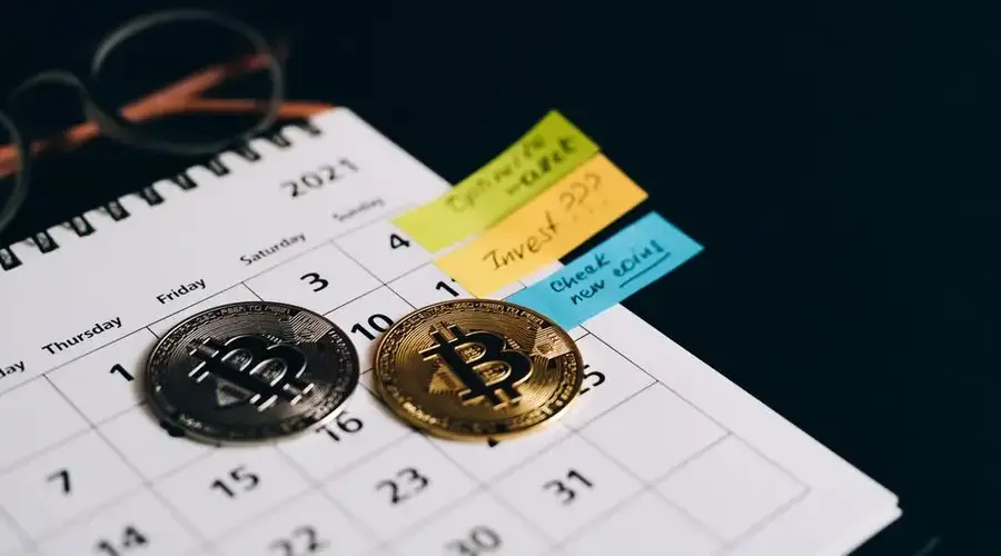 Bitcoin coins placed on a calendar with sticky notes for investment planning.