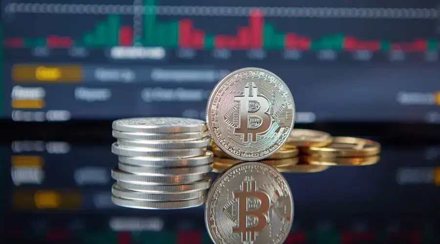 Stack of Bitcoin coins in front of a stock market graph, reflecting cryptocurrency trends.