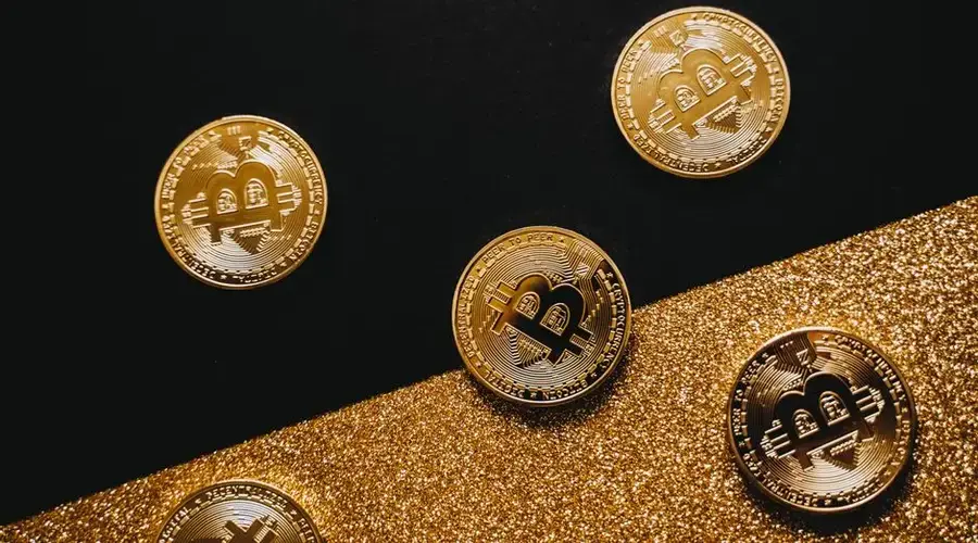 Stylish arrangement of golden Bitcoin coins on a sparkling gold glitter and black background.