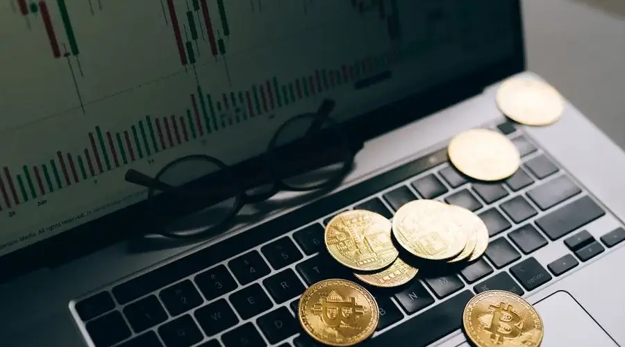 Golden Bitcoins on a laptop keyboard with a stock market chart on the screen, symbolizing cryptocurrency trading.