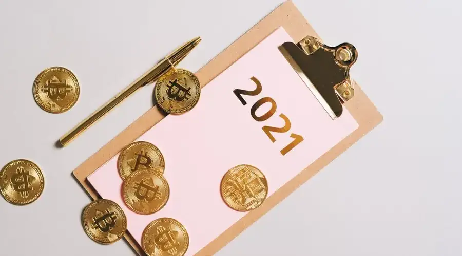 Top view of golden Bitcoin coins scattered on clipboard with 2021 text, symbolizing wealth.