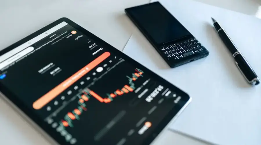 Close-up of a tablet displaying financial graphs, a smartphone, and a pen on a table.