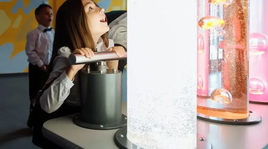Children engage with interactive science exhibit featuring colorful liquids and lights.