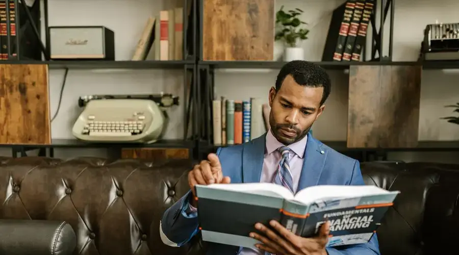 Focused businessman in a suit reading a financial planning book in office setting.