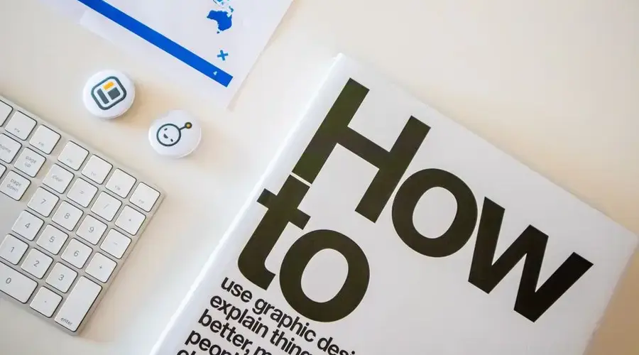 Stylish desk setup with a how-to book, keyboard, and world map on paper.