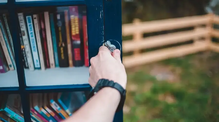 Crop unrecognizable person opening door of public bookcase filled with numerous books and located in green park