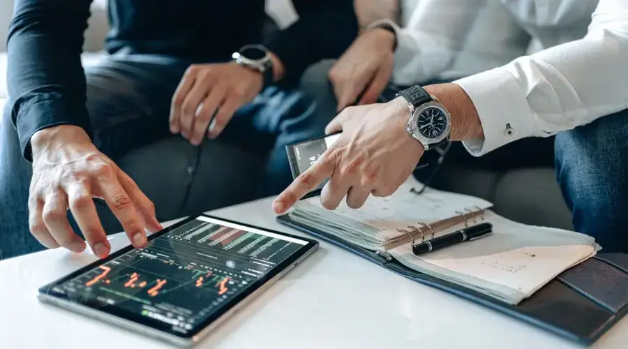 Two businessmen reviewing stock market data on a digital tablet at a white table.