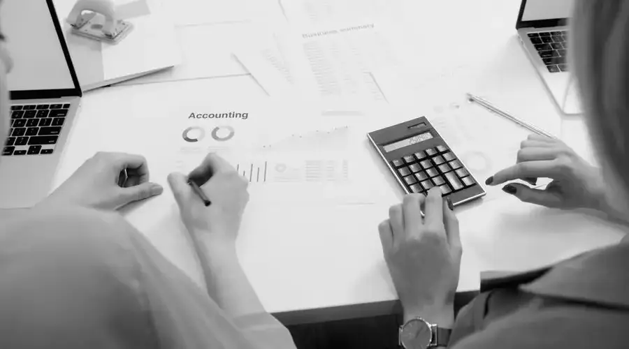 Black and white office scene featuring accounting documents, calculator, and laptops.