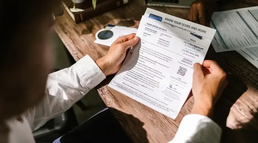 An adult man examining a financial document under natural light at a wooden desk, emphasizing finance and reading.