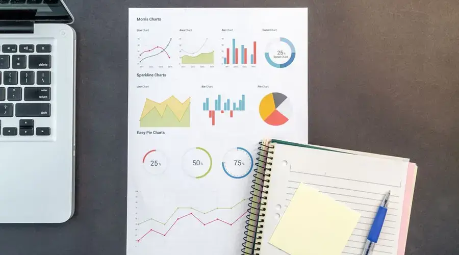 Top-down view of a desk with charts, a laptop, and notebooks, ideal for data analysis themes.
