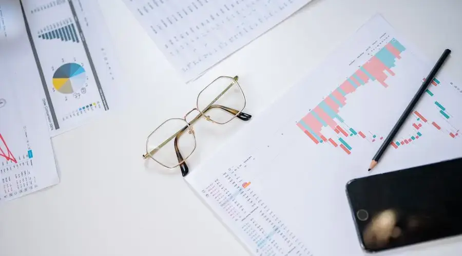 A high-angle view of business charts with eyeglasses, smartphone, and pencil on a white background.