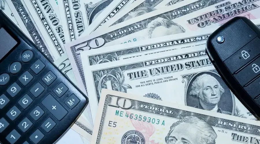 US dollars, calculator, and car keys representing finance and investment tools.