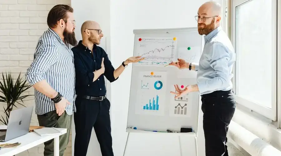 Three colleagues discussing financial charts during a business meeting in a modern office setting.