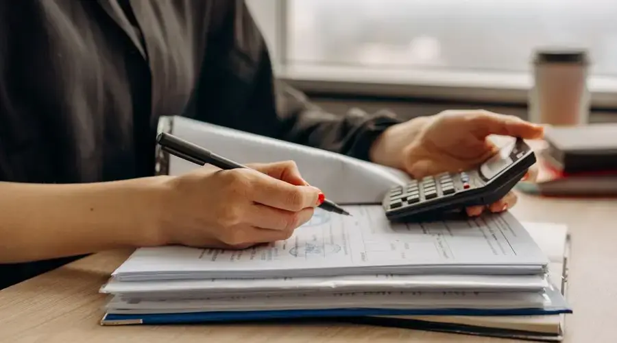 Close-up of person using a calculator with financial documents in an office.
