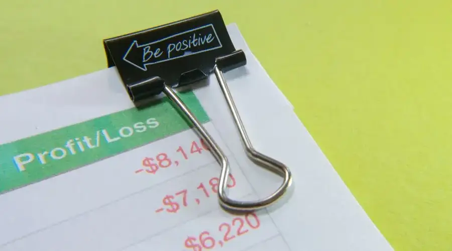 Close-up of a binder clip with 'Be Positive' message on a profit/loss statement.