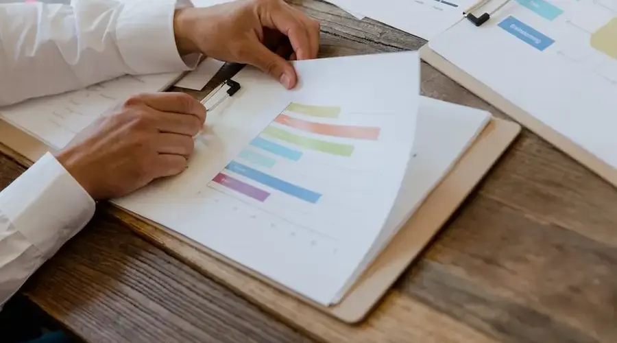 Close-up of hands reviewing business report with colorful charts and graphs on a wooden desk.