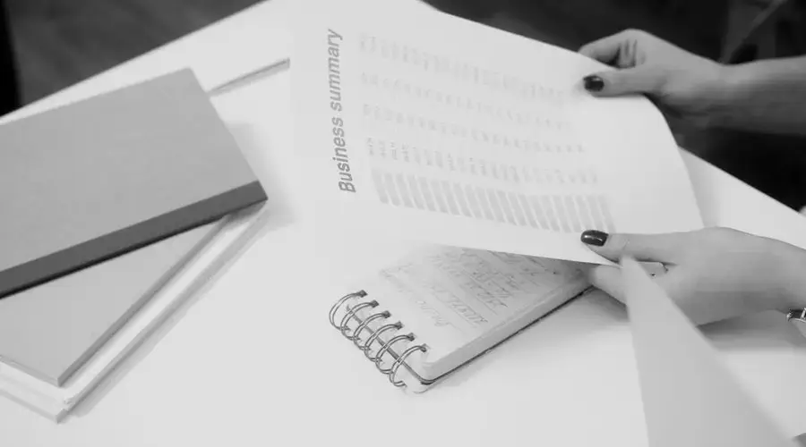Black and white image of a businesswoman reviewing a business summary on paper.