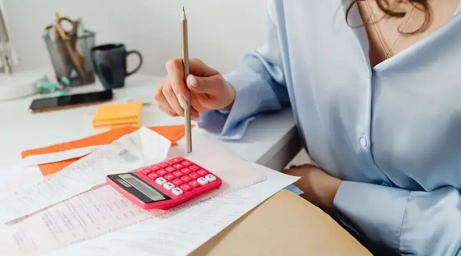 A woman is calculating expenses using a calculator and papers at her desk.