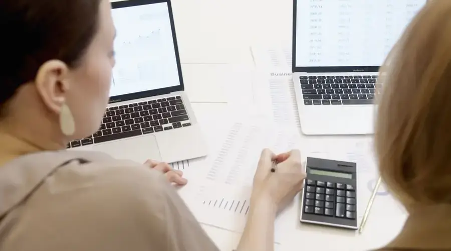 Two people analyzing business data on laptops with charts and graphs.