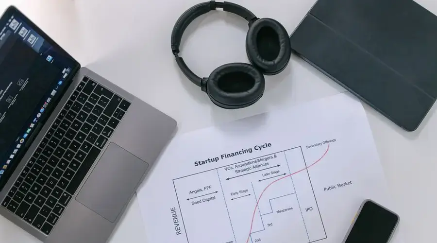 Flat lay of a modern workspace with tech gadgets and a startup financing cycle chart.