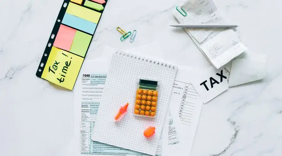 Flat lay of tax preparation essentials with calculator, forms, and colorful sticky notes.