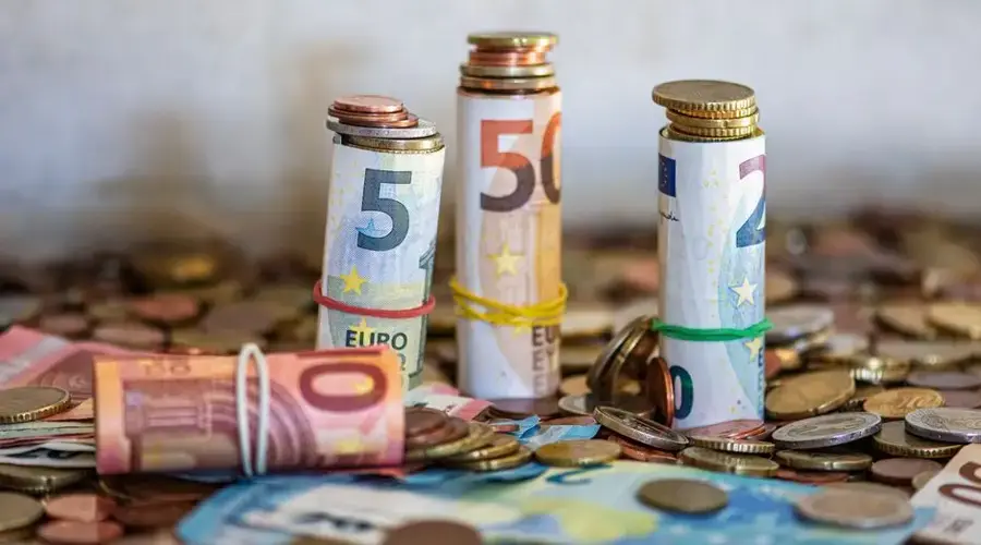 Close-up of rolled Euro banknotes and coins on a table, symbolizing finance and savings.