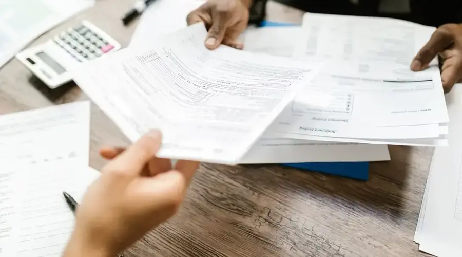 Two professionals exchanging documents in an office setting, focusing on paperwork and data analysis.