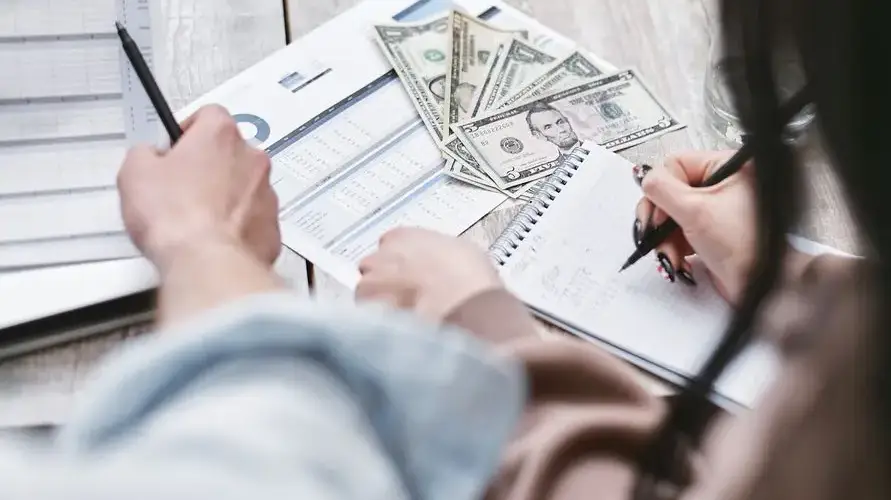 Two people working on financial documents and dollar bills for budgeting.