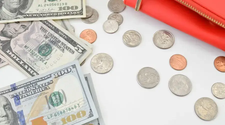 Detailed image of US dollars and coins spread with a red wallet on a white surface, ideal for financial concepts.