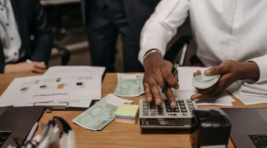 Professional setting with people handling cash and calculations using a calculator at a desk.