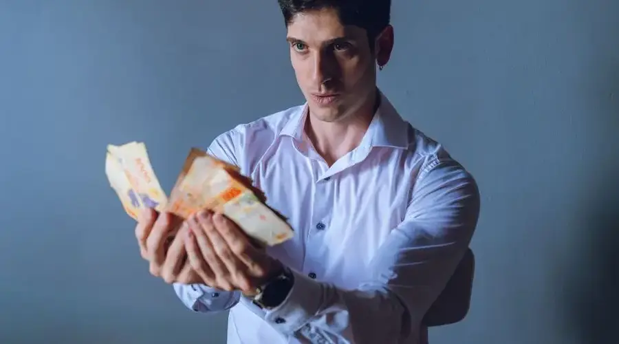 A focused adult man counts Argentina pesos indoors, against a neutral backdrop.
