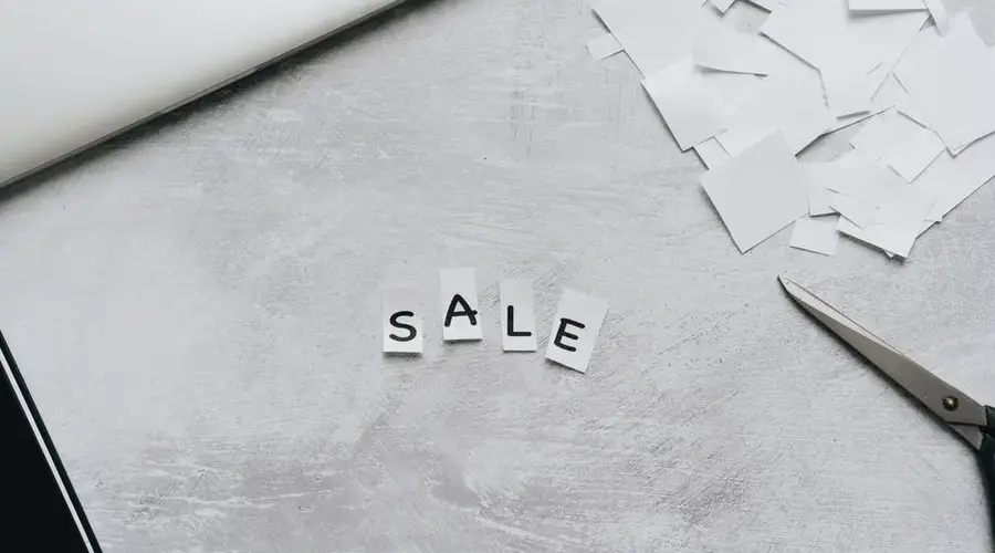 Overhead view of cut-out letters spelling 'Sale' on a desk with scattered paper and scissors.