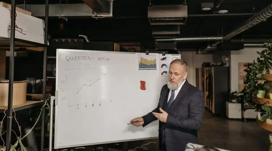 Businessman in suit presenting a quarterly report on a whiteboard in an office setting.