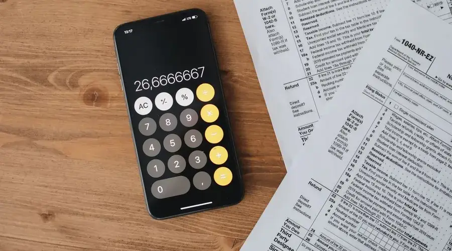 Overhead view of smartphone calculator and tax forms on a wooden table.