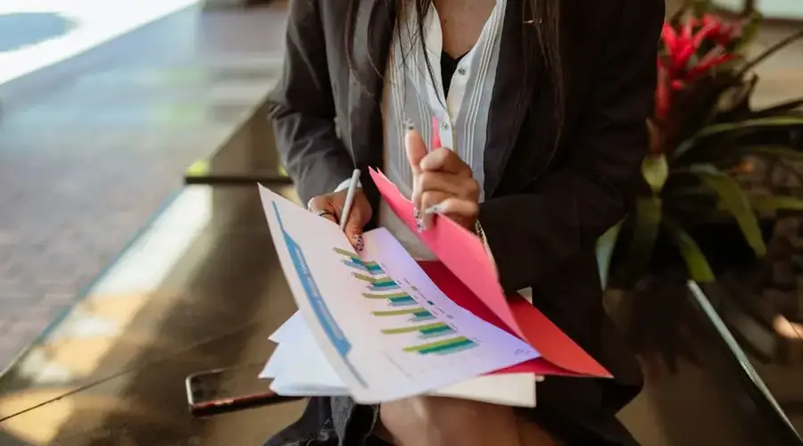 A woman in a blazer sits outside reviewing sales documents, highlighting analysis.