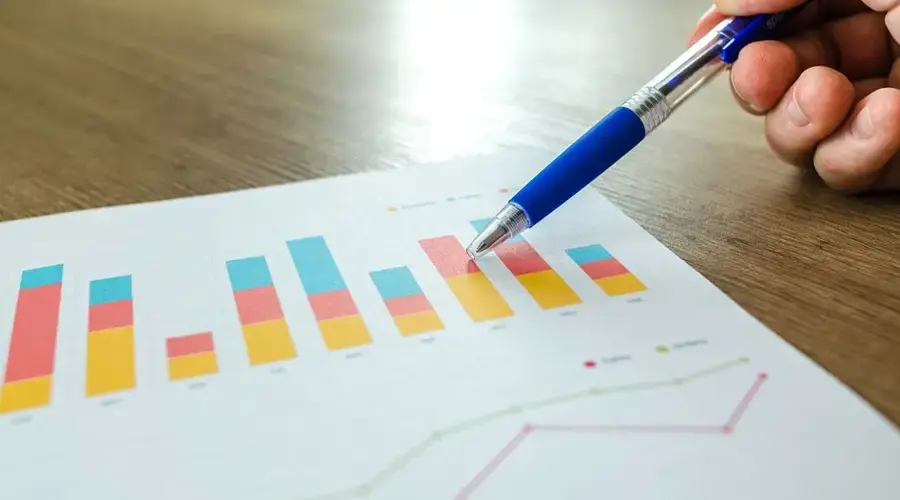 Detailed close-up of a hand pointing at colorful charts with a blue pen on wooden surface.