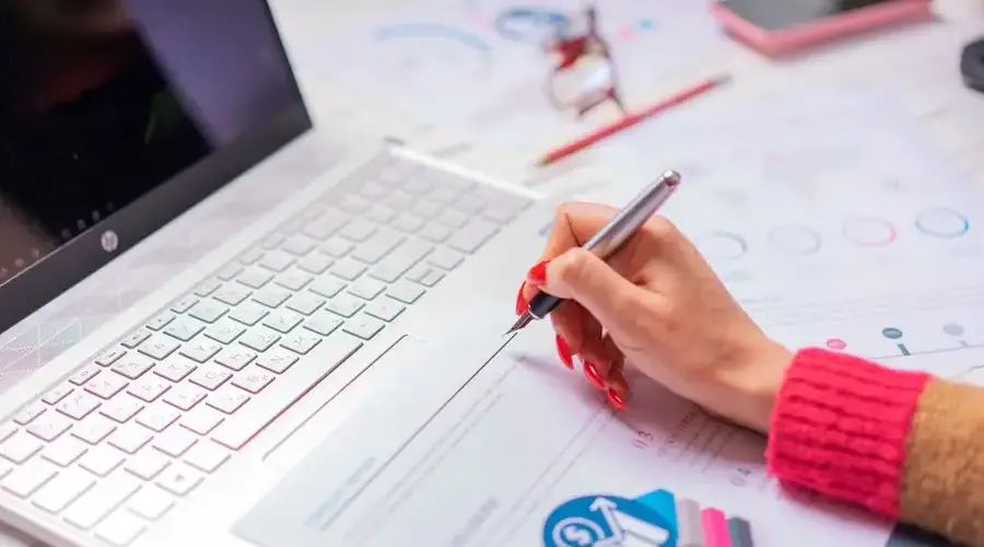 A person analyzes financial data and diagrams on a laptop and paper at a desk, highlighting office work.
