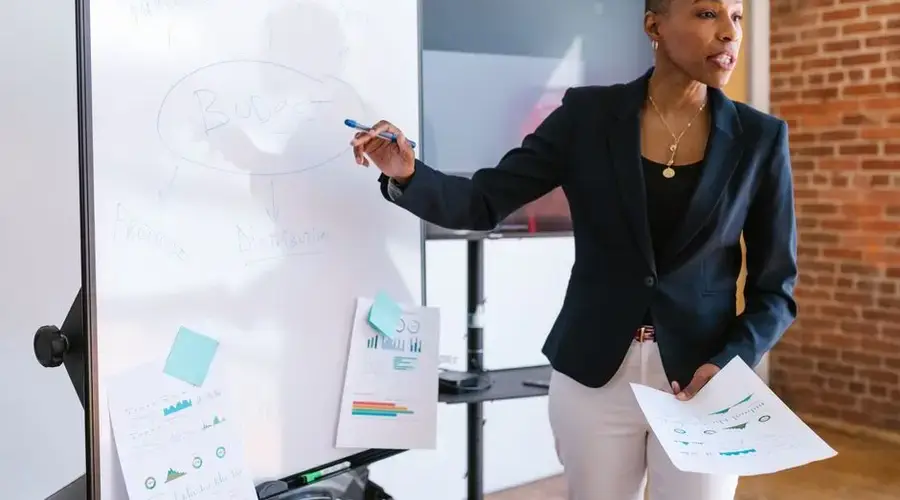 Professional businesswoman explaining budget strategy on a whiteboard during a meeting.