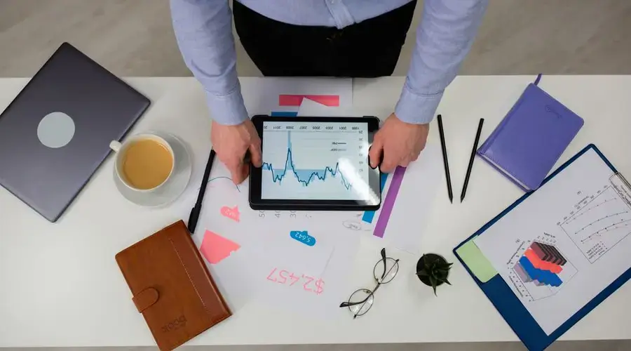 Overhead view of businessman using tablet to review data charts at a modern office desk.