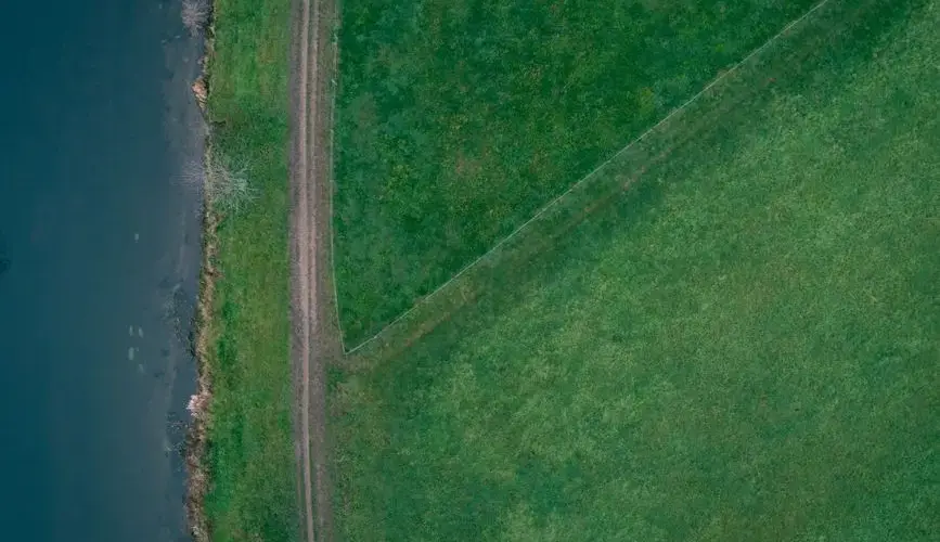 Aerial view of lush green fields and a winding path along a water body in Germany.