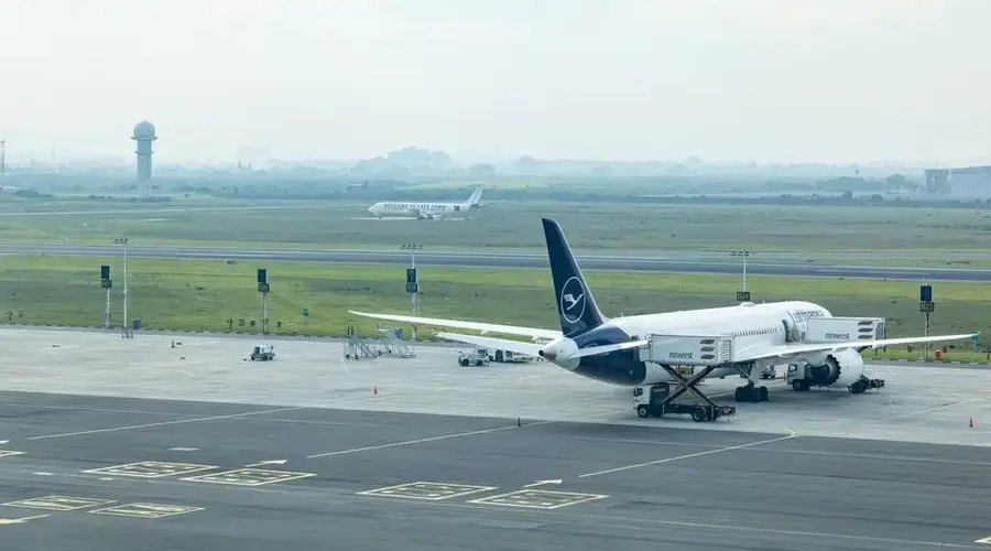 Wide view of commercial airplanes stationed on the airport tarmac with a misty runway backdrop.