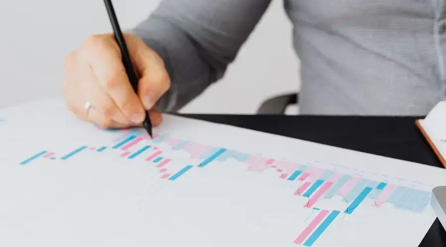 Close-up of a man writing on a printed chart indoors, analyzing colorful data.