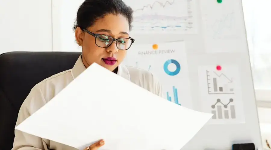 An African American woman studying financial charts and graphs in an office.