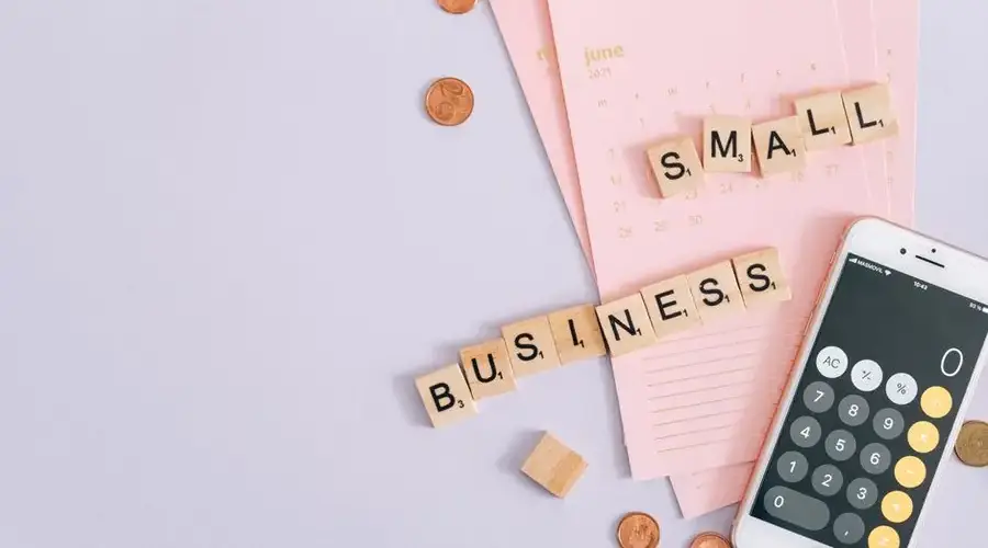 A top view image of small business tools including a calendar, coins, and a smartphone calculator.
