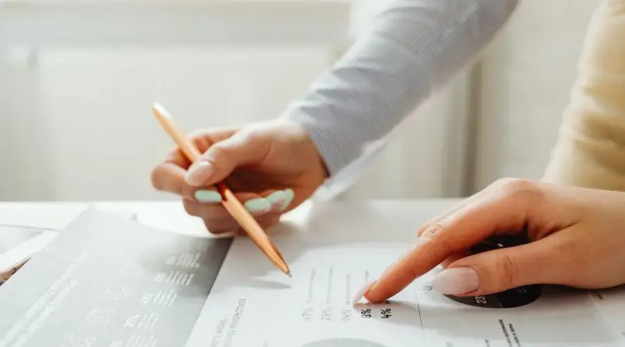 Hands holding a pencil, analyzing charts and data sheets, suggesting teamwork in an office setting.